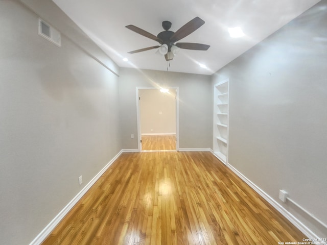 empty room featuring built in shelves, light hardwood / wood-style floors, and ceiling fan