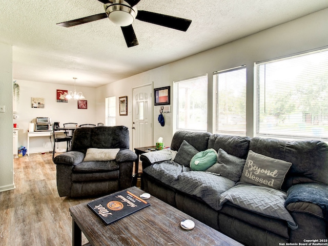 living room featuring light hardwood / wood-style flooring, a textured ceiling, and ceiling fan with notable chandelier