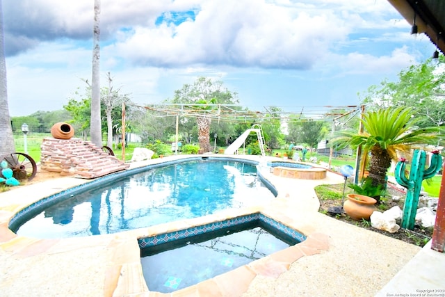 view of pool with a water slide and an in ground hot tub