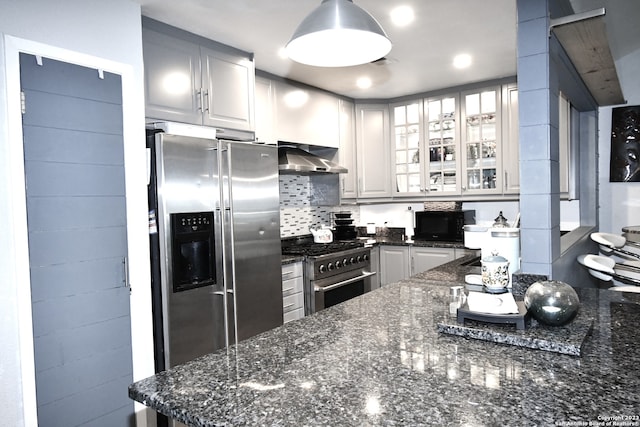 kitchen with appliances with stainless steel finishes, wall chimney range hood, dark stone countertops, and white cabinets