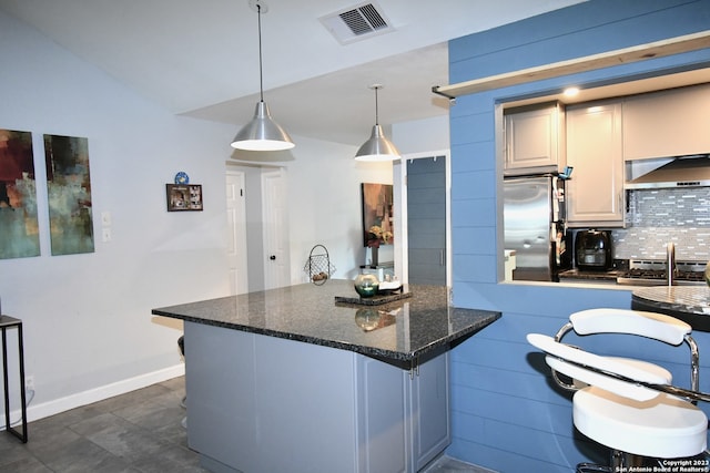 kitchen with wall chimney range hood, dark stone counters, vaulted ceiling, tasteful backsplash, and appliances with stainless steel finishes