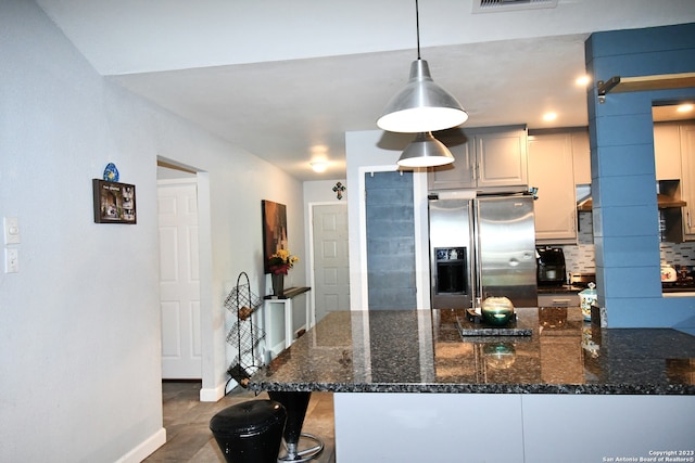 kitchen with hanging light fixtures, dark stone countertops, backsplash, a barn door, and stainless steel refrigerator with ice dispenser