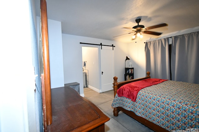 bedroom featuring a barn door, light tile floors, ensuite bath, and ceiling fan