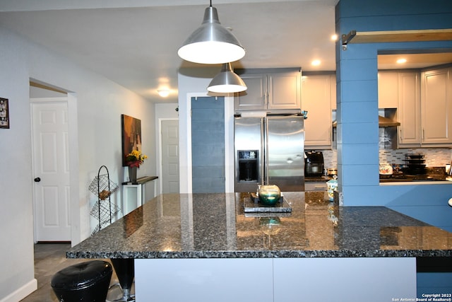 kitchen with dark stone counters, backsplash, decorative light fixtures, a barn door, and stainless steel refrigerator with ice dispenser