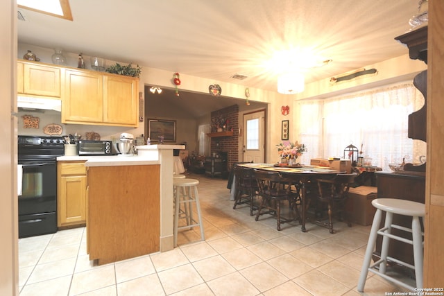 kitchen featuring a kitchen breakfast bar, black electric range oven, light tile flooring, and a fireplace