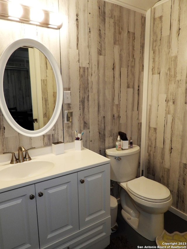 bathroom featuring wooden walls, toilet, and vanity