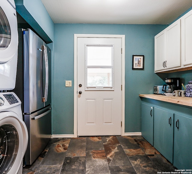 laundry room with dark tile floors and stacked washing maching and dryer