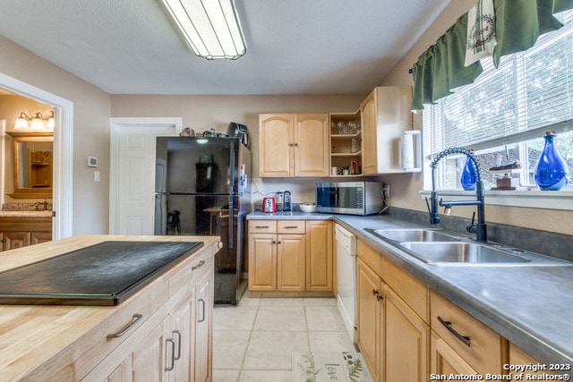 kitchen featuring sink, light tile floors, white dishwasher, light brown cabinets, and black fridge