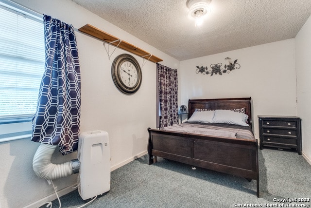 bedroom with a textured ceiling, dark carpet, and multiple windows