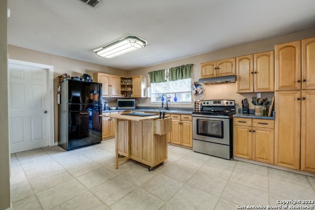 kitchen featuring black refrigerator, a kitchen breakfast bar, light tile floors, stainless steel range with electric stovetop, and a kitchen island