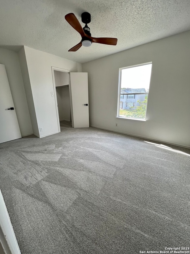 unfurnished bedroom featuring light colored carpet, a walk in closet, ceiling fan, a textured ceiling, and a closet