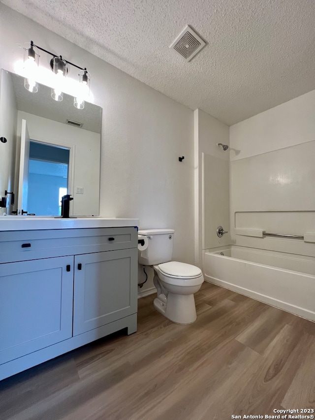 full bathroom featuring toilet, washtub / shower combination, a textured ceiling, vanity, and hardwood / wood-style flooring