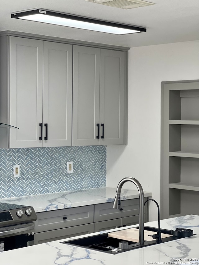 kitchen featuring gray cabinetry, electric range, sink, light stone counters, and tasteful backsplash