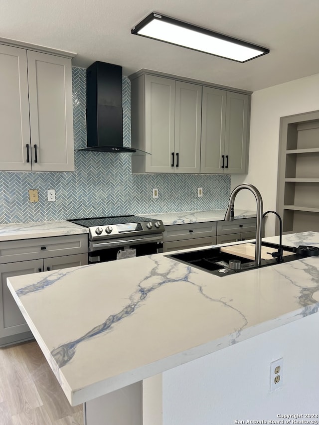 kitchen featuring stainless steel electric range, light stone counters, gray cabinetry, light hardwood / wood-style floors, and wall chimney exhaust hood