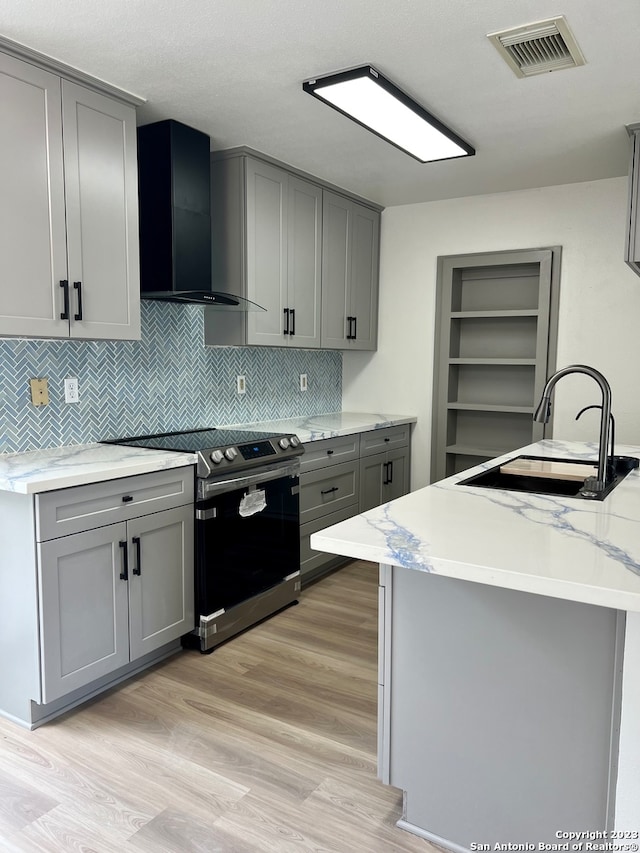 kitchen with sink, light wood-type flooring, stainless steel range with electric stovetop, wall chimney exhaust hood, and gray cabinets