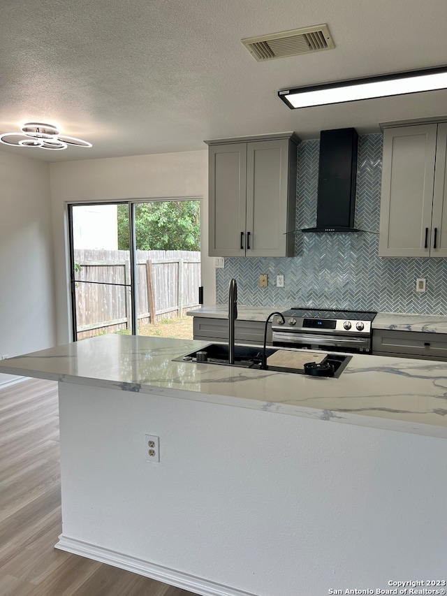 kitchen with electric stove, gray cabinetry, light stone counters, and wall chimney range hood