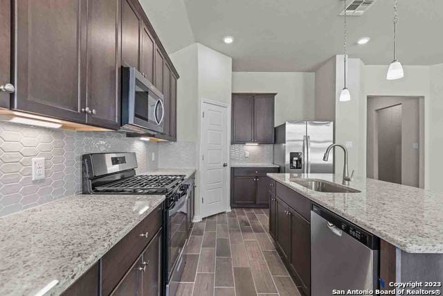 kitchen with decorative light fixtures, light stone countertops, sink, and appliances with stainless steel finishes