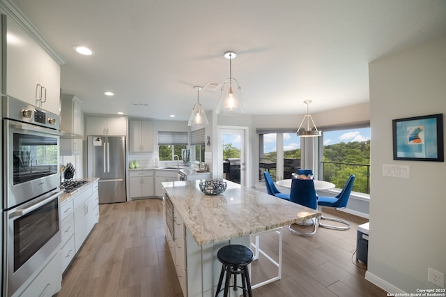 kitchen featuring backsplash, appliances with stainless steel finishes, light hardwood / wood-style floors, white cabinets, and pendant lighting