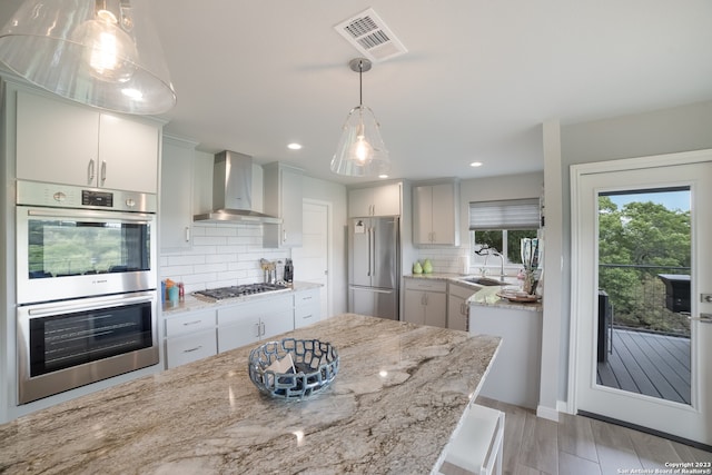 kitchen featuring backsplash, wall chimney exhaust hood, hanging light fixtures, and stainless steel appliances