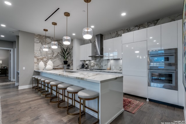 kitchen with decorative light fixtures, dark wood-type flooring, wall chimney exhaust hood, appliances with stainless steel finishes, and white cabinets