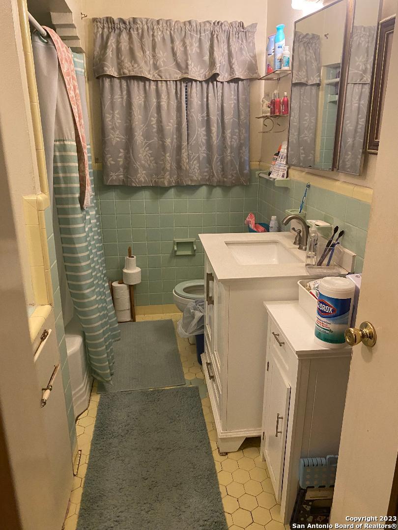 full bathroom with toilet, shower / tub combo with curtain, vanity, tile walls, and tile floors