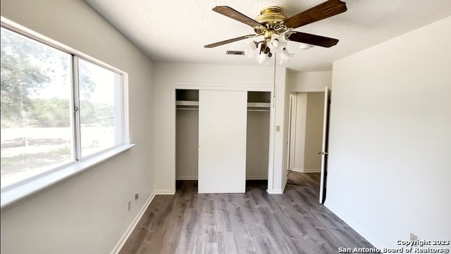 unfurnished bedroom with a closet, multiple windows, light hardwood / wood-style floors, and ceiling fan