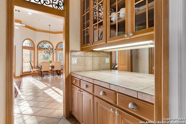 kitchen featuring pendant lighting, crown molding, light tile flooring, tasteful backsplash, and a notable chandelier