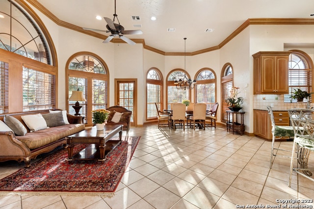 tiled living room with crown molding, ceiling fan with notable chandelier, and a wealth of natural light