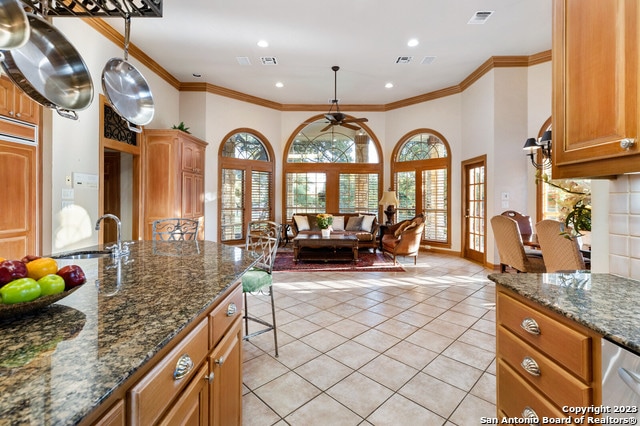 kitchen featuring crown molding, ceiling fan, light tile floors, and dark stone countertops