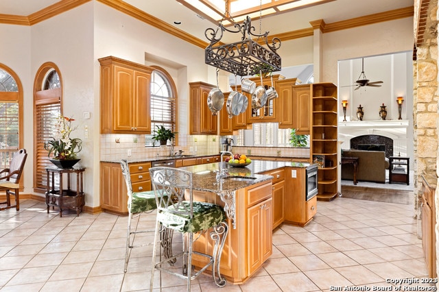 kitchen with stone counters, ceiling fan with notable chandelier, a kitchen island with sink, plenty of natural light, and tasteful backsplash