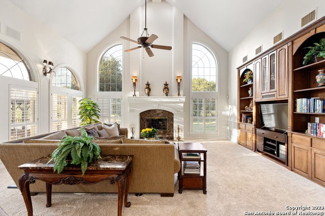 living room featuring a premium fireplace, high vaulted ceiling, ceiling fan, and light colored carpet