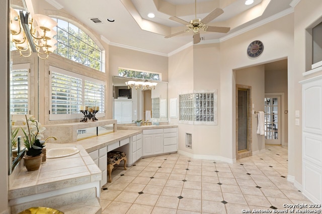 bathroom featuring a tray ceiling, oversized vanity, ceiling fan with notable chandelier, and ornamental molding