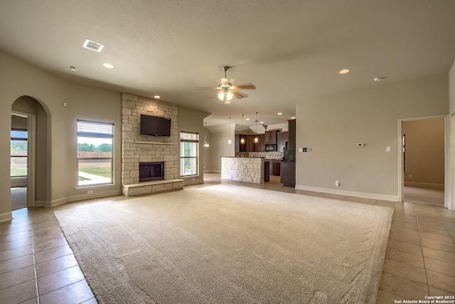 unfurnished living room featuring ceiling fan, a stone fireplace, light tile floors, and a textured ceiling