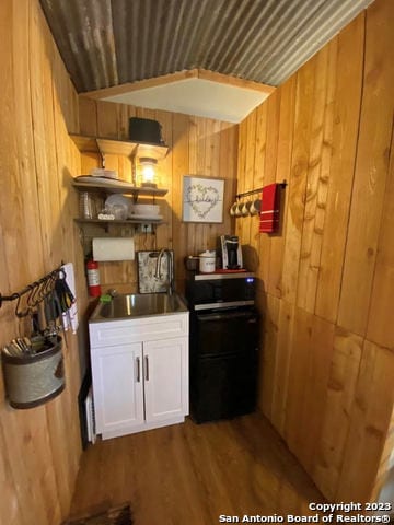 kitchen with hardwood / wood-style floors, sink, white cabinets, wood walls, and wood ceiling