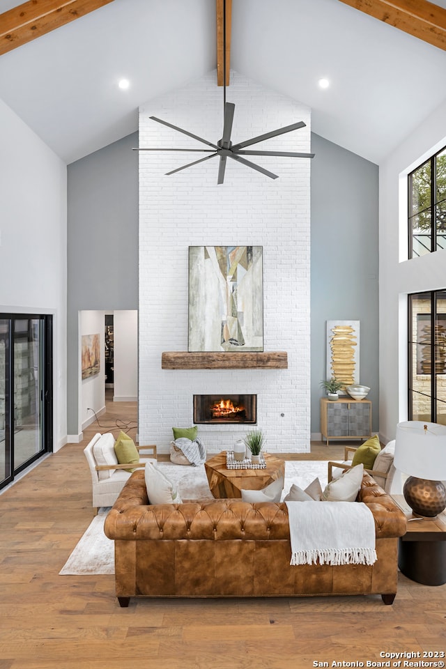 living room featuring beamed ceiling, ceiling fan, a brick fireplace, light wood-type flooring, and high vaulted ceiling