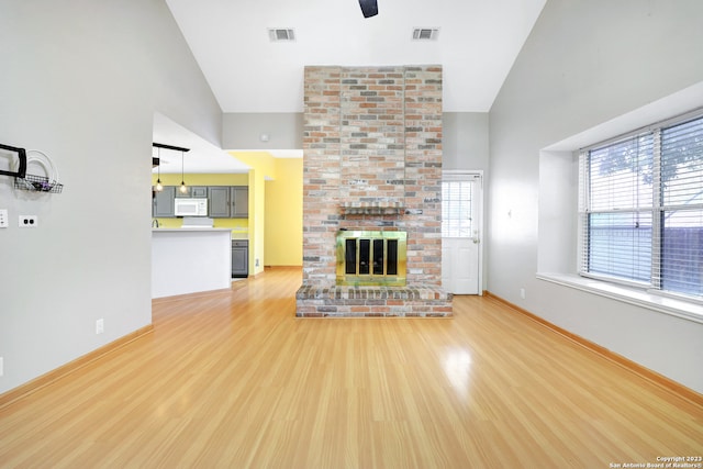 unfurnished living room featuring a fireplace, light hardwood / wood-style flooring, brick wall, and high vaulted ceiling