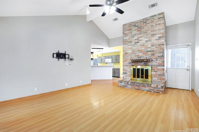 unfurnished living room featuring ceiling fan, brick wall, a fireplace, and light wood-type flooring