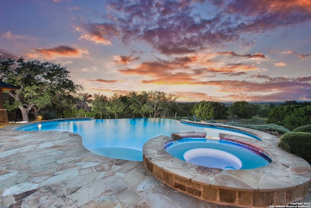 pool at dusk featuring an in ground hot tub