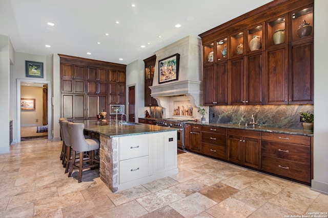 kitchen featuring backsplash, a center island with sink, premium range hood, and range with two ovens