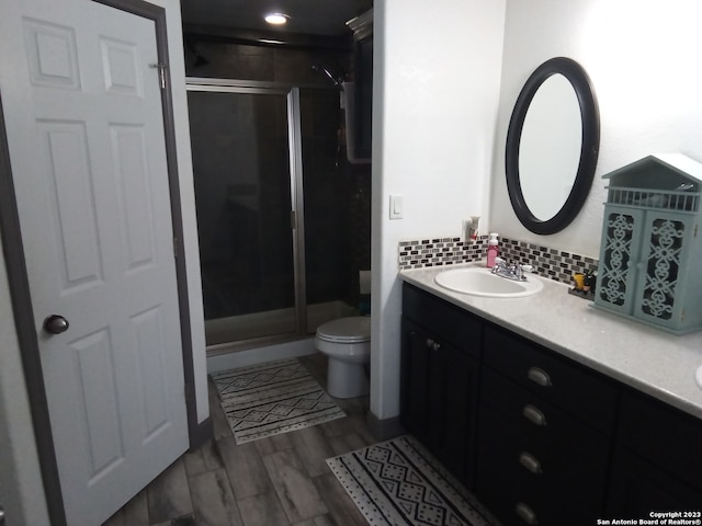 bathroom with toilet, tasteful backsplash, wood-type flooring, vanity, and a shower with door