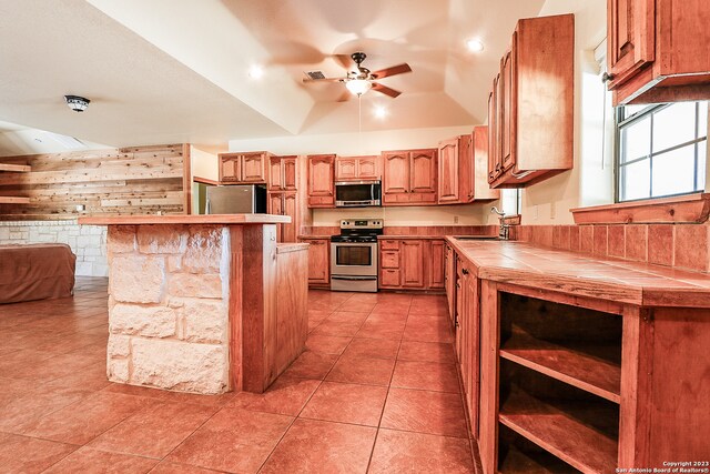 kitchen with ceiling fan, light tile floors, stainless steel appliances, tile countertops, and lofted ceiling