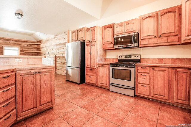 kitchen featuring light tile floors, appliances with stainless steel finishes, and wood walls