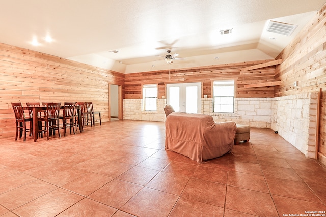 living room featuring wooden walls, ceiling fan, light tile flooring, a textured ceiling, and lofted ceiling