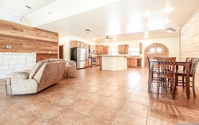 dining area featuring ceiling fan, wood walls, lofted ceiling, and light tile flooring