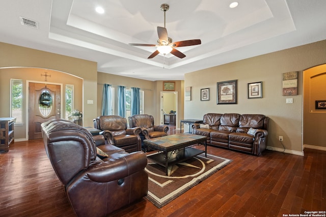 living room with dark hardwood / wood-style flooring, ceiling fan, and a raised ceiling