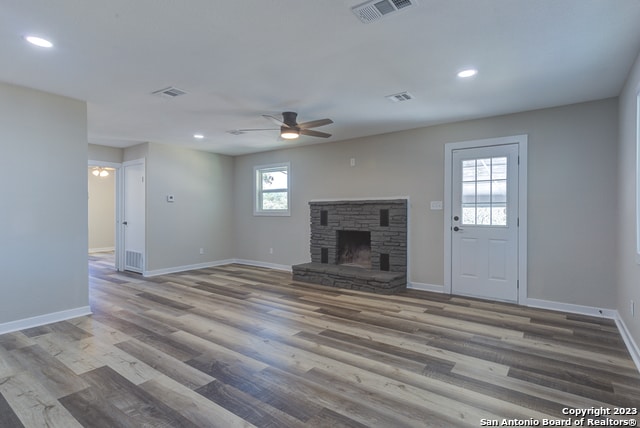 unfurnished living room featuring dark hardwood / wood-style flooring, ceiling fan, a stone fireplace, and a healthy amount of sunlight