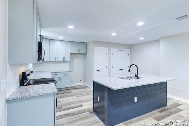 kitchen with light wood-type flooring, tasteful backsplash, an island with sink, white range, and sink