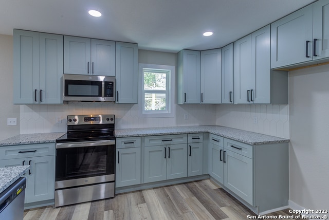 kitchen featuring tasteful backsplash, stainless steel appliances, light stone countertops, and light wood-type flooring