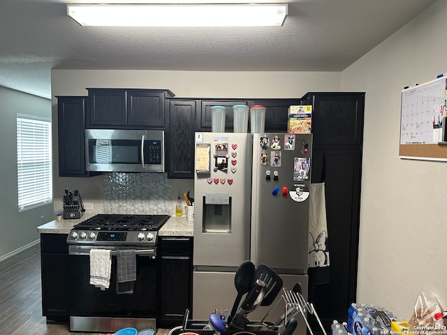 kitchen with appliances with stainless steel finishes, backsplash, hardwood / wood-style flooring, and light stone counters