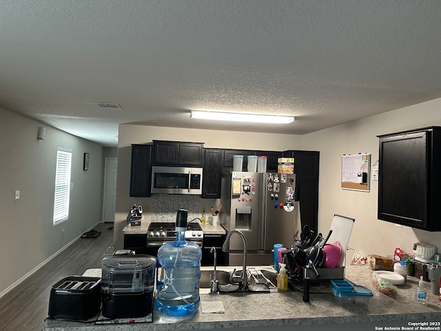 kitchen featuring hardwood / wood-style flooring, backsplash, appliances with stainless steel finishes, and a textured ceiling